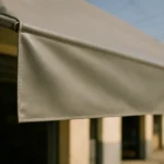 Tecido de lona para toldo esticado em estrutura de alumínio, com textura da fibra em foco e prédio comercial desfocado ao fundo